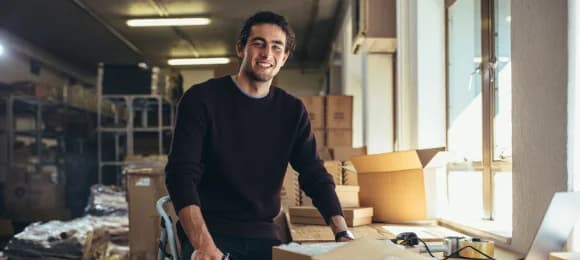 A small business owner at a packing table with boxes in a bright warehouse