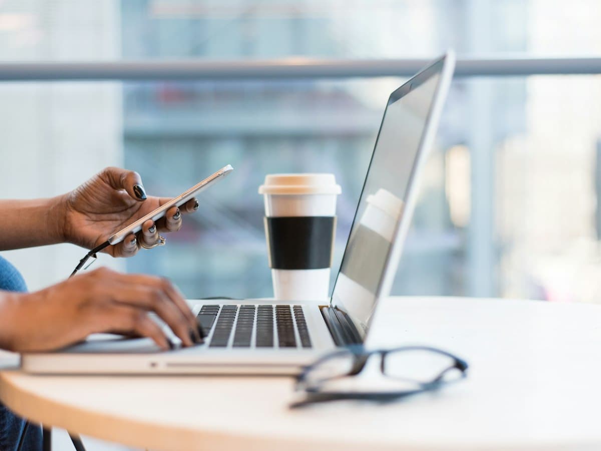 Hands on a phone and laptop at a bright office desk
